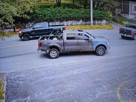 a four-door pickup truck captured on a surveillance camera. The truck appears grey and light blue, has a sunroof and items in the back, including a lawn mower.