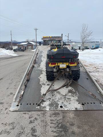 A yellow ATV sits on the back of a flat bed tow truck;