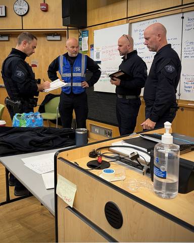 Four officers stand in a classroom with a whiteboard behind them