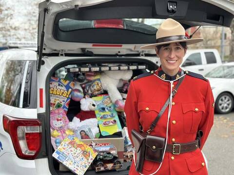 RCMP officer in Red Serge standing in front of a police vehicle filled with toys