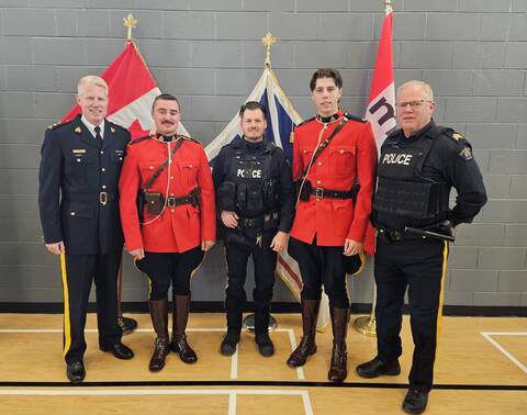 A group of RCMP officers stand together in front of flags at a ceremony for recognition of impaired driving arrests.