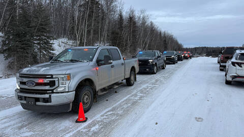 Police vehicles line at the side of a road in winter. | Des véhicules de police alignés au bord d'une route en hiver.