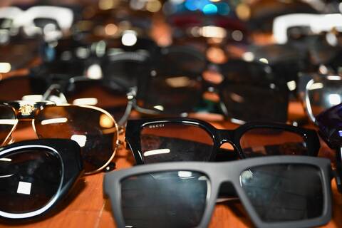 Numerous high-end glasses and sunglasses bunched together on a wooden floor.