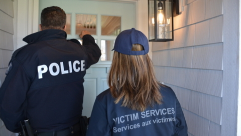 Un policier et une agente des Services aux victimes devant la porte d’entrée d’une maison.