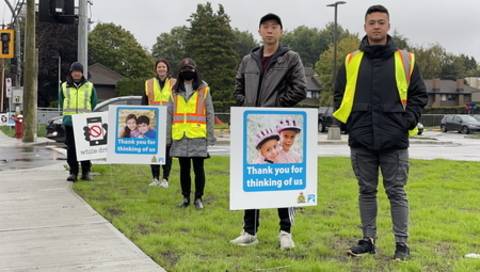 Des bénévoles debout sur le bord de la route à côté de pancartes sur lesquelles on voit des visages d’enfants et le message « Merci de penser à nous ».