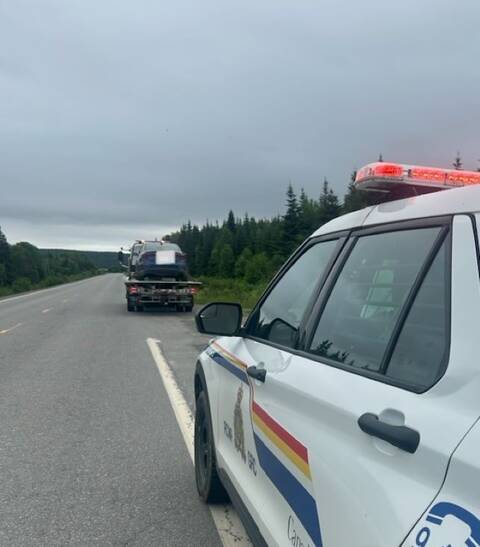 A car loaded on the back of a tow truck. An RCMP SUV with its lights on appears in the foreground.