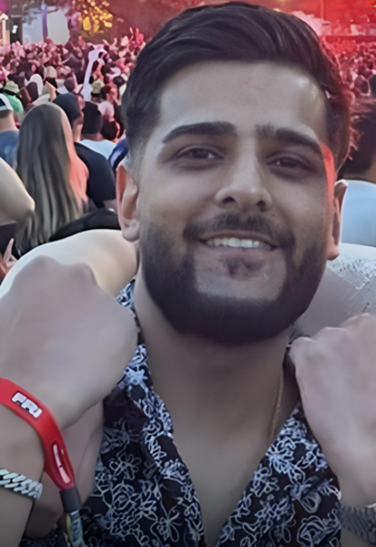 Man with dark hair and short beard. Wearing a black shirt with white detail.